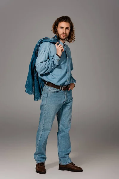 Przystojny Stylowy Mężczyzna Dżinsowej Koszuli Dżinsach Trzymając Kurtkę Szarym Tle — Zdjęcie stockowe