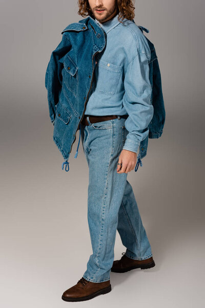 cropped view of stylish man in denim shirt and jeans holding jacket on grey background 