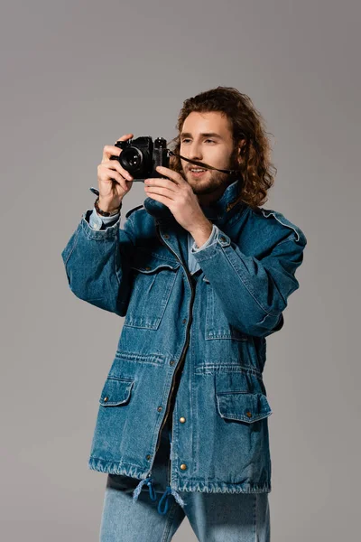 デニムジャケットとジーンズのハンサムなスタイリッシュな男がグレーで隔離された写真を撮る — ストック写真