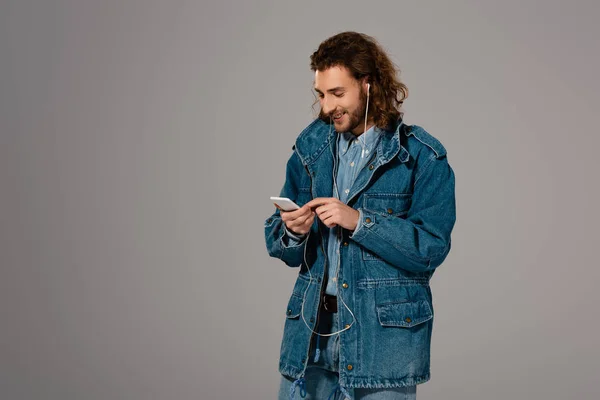 Улыбающийся Человек Джинсовой Куртке Используя Смартфон Слушая Музыку Изолированную Сером — стоковое фото