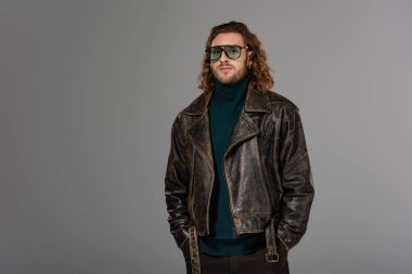 Deri ceketli yakışıklı adam gri kameraya bakıyor. 