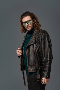 Deri ceketli yakışıklı adam gri kameraya bakıyor. 