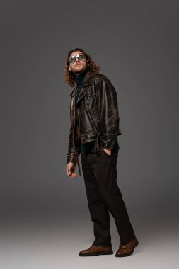 Deri ceketli yakışıklı adam, el ele tutuşup gri arka plana bakıyor. 