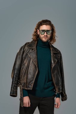 Deri ceketli yakışıklı adam gri kameraya bakıyor.