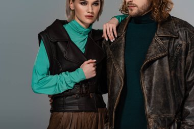 Gri renkte, deri ceketli, yelekli adama dokunan kadın görüntüsü.