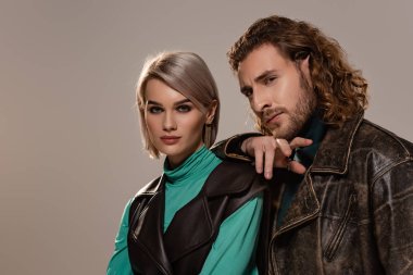 Yelekli kadın ve deri ceketli adam gri kameraya bakıyor.
