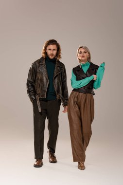 Yelekli kadın ve gri arka planda yürüyen deri ceketli adam. 
