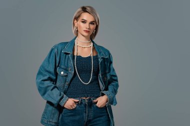 Kot ceketli, elleri cebinde, gri renkli kameraya bakan çekici bir kadın. 