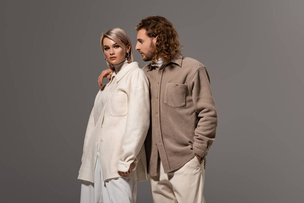 man in shirt hugging and looking at woman in white coat isolated on grey