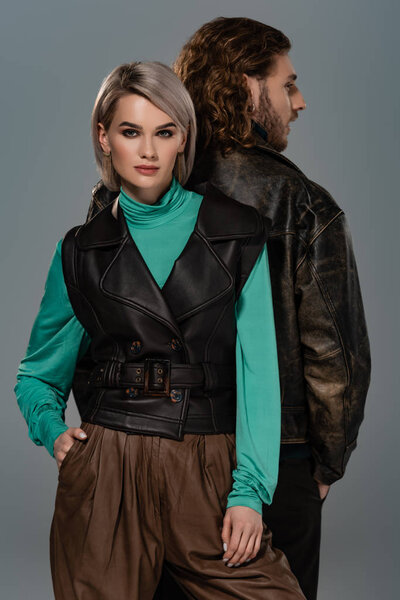 привлекательная женщина в жилете и мужчина в кожаной куртке изолированы на сером
