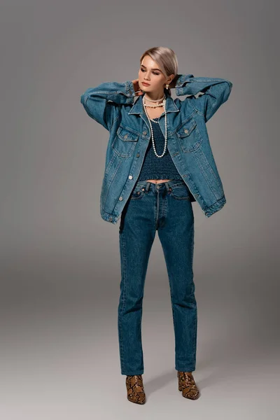 attractive woman in denim jacket and jeans looking away on grey background