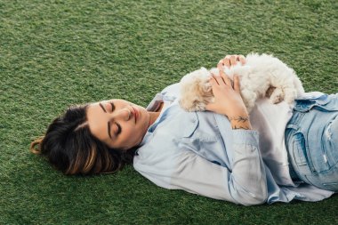 high angle view of woman holding Havanese puppy and lying on grass 
