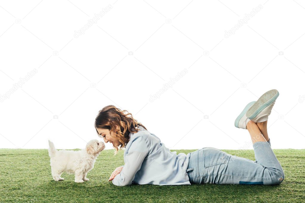 side view of woman looking at Havanese puppy and lying on grass isolated on white