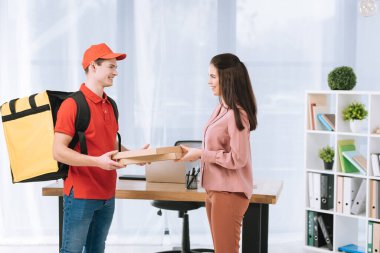 Ofisteki gülümseyen iş kadınına pizza kutuları dağıtan teslimatçının yan görüntüsü.