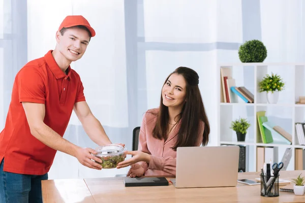 Delivery Man Holding Salad Container Smiling Camera Businesswoman Table — Stock Photo, Image