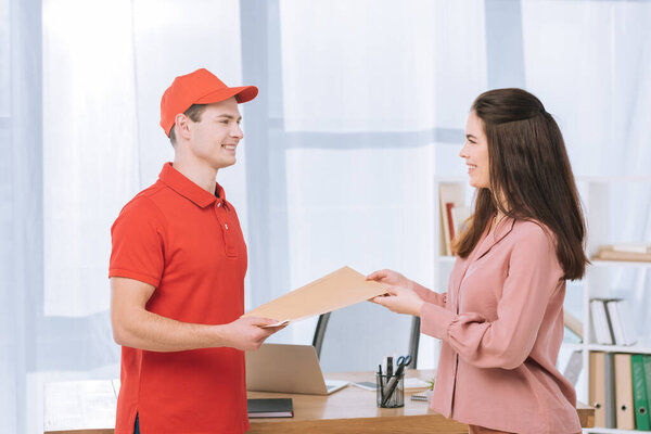 Side view of delivery man giving envelope to smiling businesswoman in office 