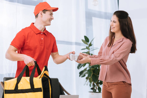 Smiling delivery man with thermo bag giving food container to attractive girl at home