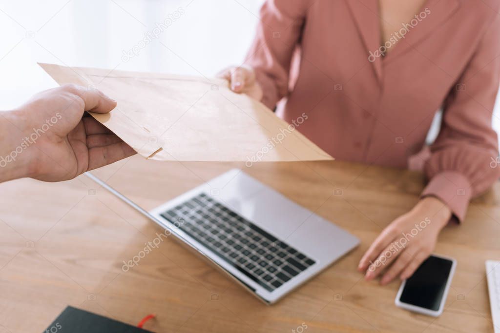 Cropped view of courier giving envelope to businesswoman at table 