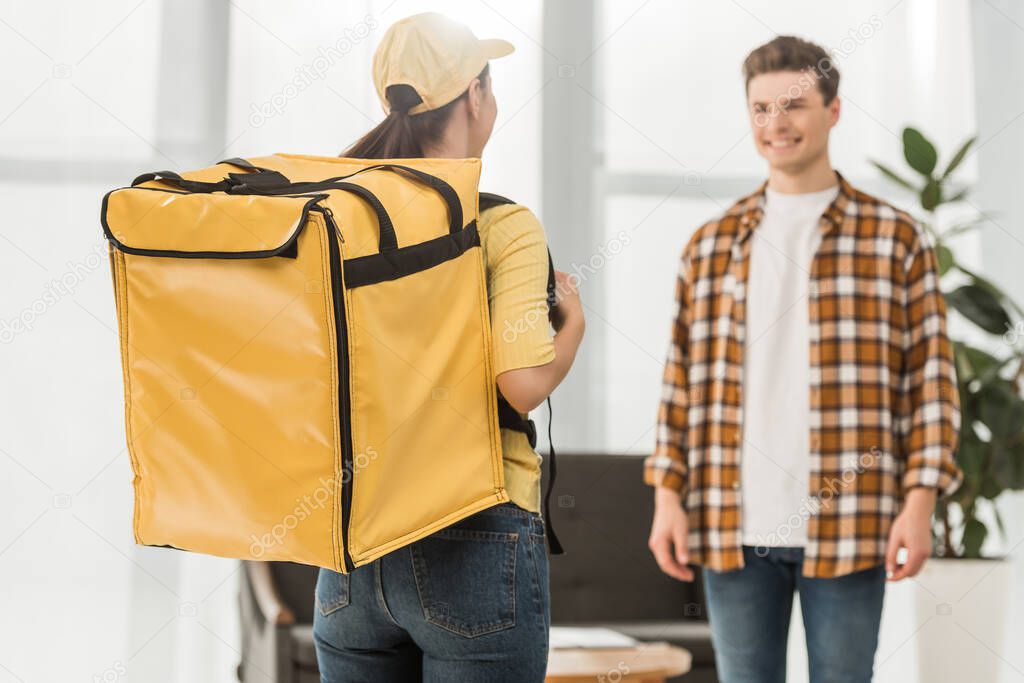 Selective focus of courier with thermo backpack and smiling man at home