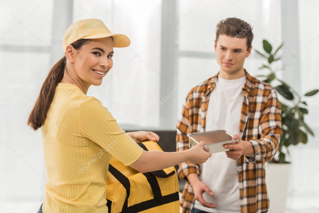 Selective focus of courier smiling at camera while giving food container to man 