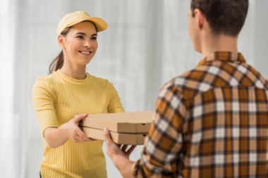 Gülümseyen kuryenin seçici odak noktası pizza kutularını adama vermek. 