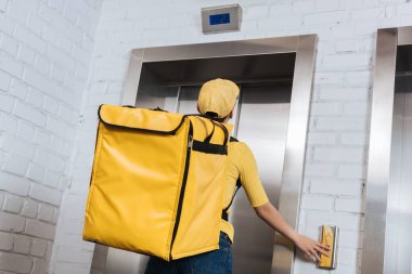 Termo sırt çantalı kuryenin asansör düğmesine basma görüntüsü