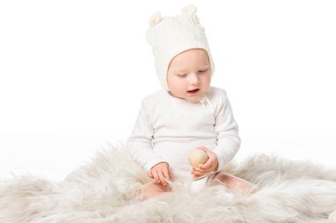 Bebek şapkası takan, elinde paskalya yumurtası tutan, beyaz kürklü, ağzı açık bir çocuk. 