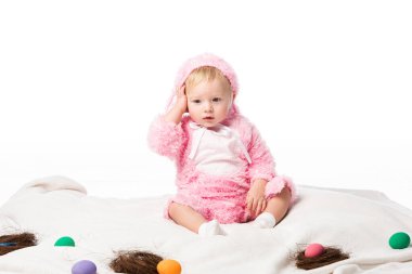 Upset child wearing rabbit costume, touching head on blanket with colorful decoration isolated on white  clipart