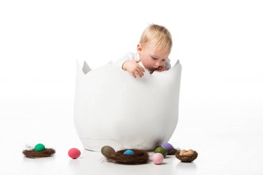 Cute child looking at nests and easter eggs from eggshell on white background clipart