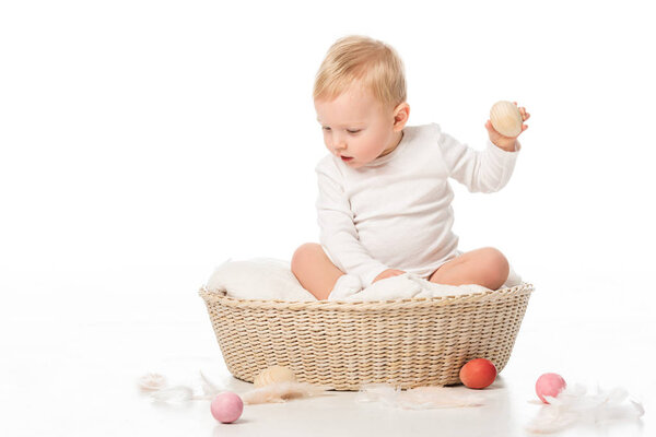 Ребенок держит пасхальное яйцо, смотрит вниз с открытым ртом в корзине на белом фоне

