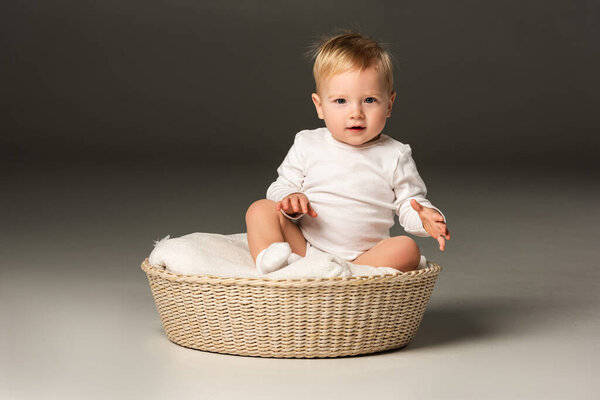 Cute child looking at camera, sitting on blanket in basket on black background