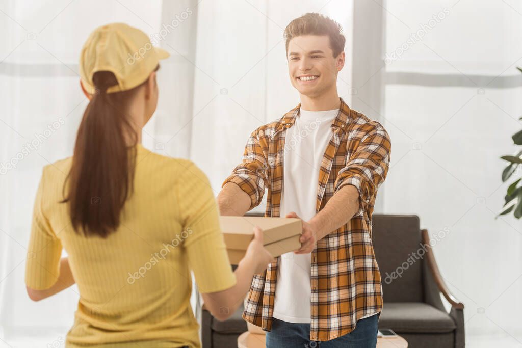 Selective focus of smiling man taking pizza boxes from courier at home