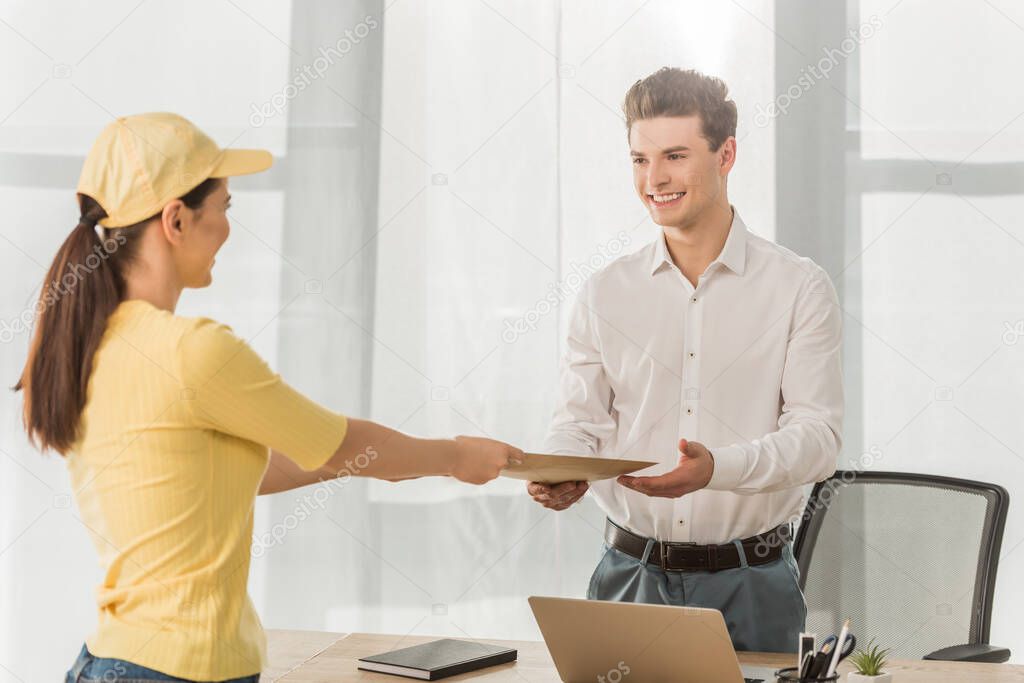 Selective focus of courier in yellow uniform giving envelope to smiling businessman in office