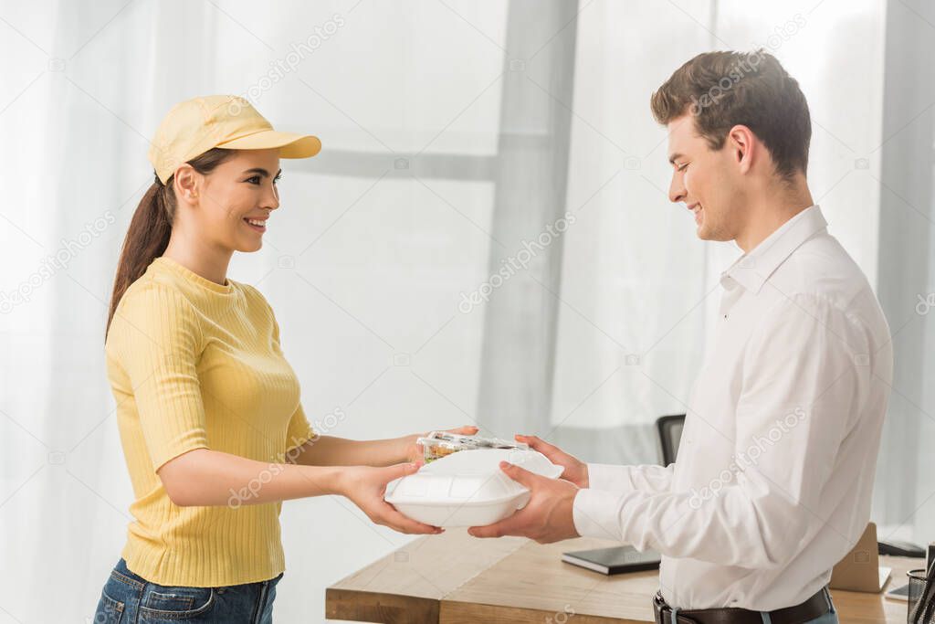 Side view of courier giving food containers to smiling businessman in office