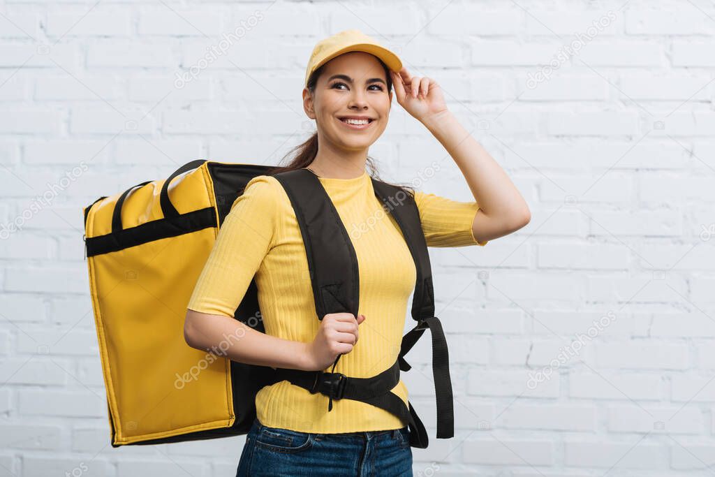 Courier with thermo backpack smiling away near brick wall