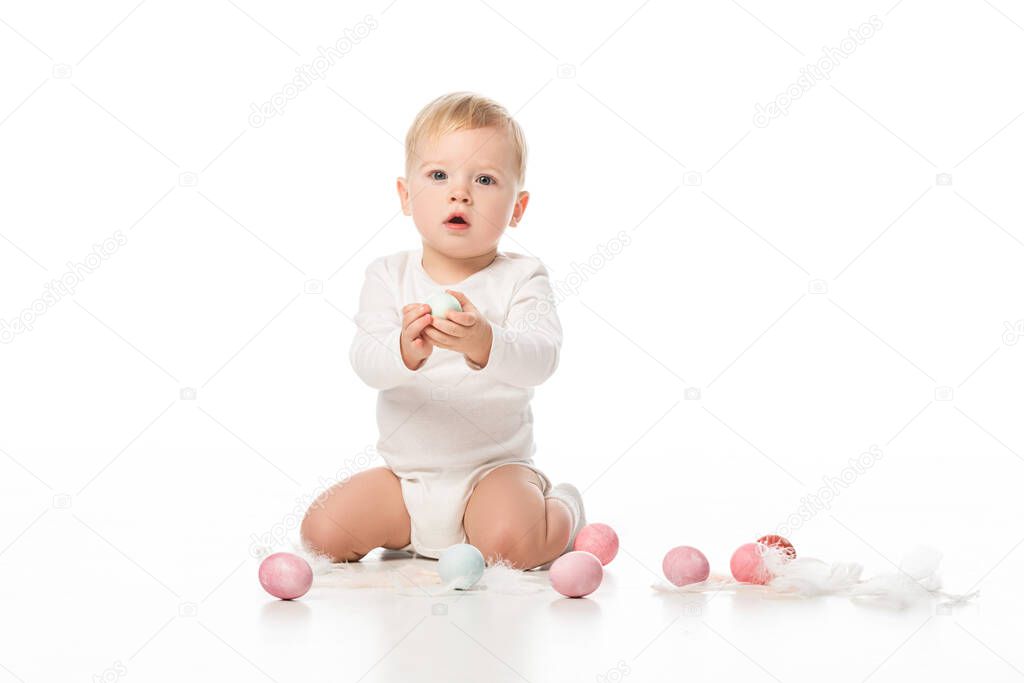 Child with open mouth, holding Easter egg and looking at camera on white background