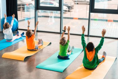 Beden eğitiminde spor paspasları üzerinde çalışan elleri havada çocukların arka görünüşü