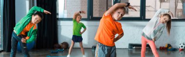 Selective focus of multicultural children warming up on fitness mats in gym, panoramic shot clipart