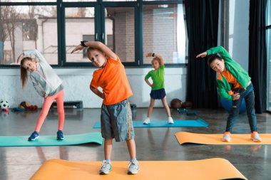 Çok kültürlü çocukların seçici odağı spor salonundaki spor minderleri üzerinde ısınıyor.
