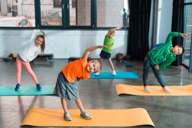 Multicultural kids warming up together on fitness mats in gym clipart