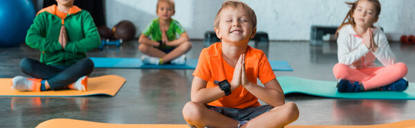 Selective focus of children with clenched hands and crossed legs on fitness mats, panoramic shot