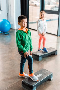 Çok ırklı çocukların spor salonundaki adım platformlarında çalışmalarının yüksek açılı görüntüsü