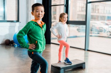 Seçici odak noktası elleri kalçalarında çok kültürlü çocukların spor salonunda adım platformları üzerinde egzersiz yapmaları.
