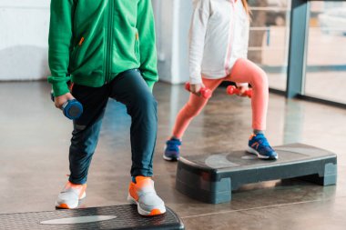 Cropped view of children holding dumbbells and working out on step platforms clipart
