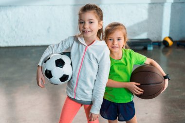 Spor salonunda gülümseyen ve top tutan çocukların önünde.