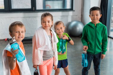 Havluları olan çok kültürlü çocuklar spor salonunda spor şişelerini tutuyorlar.