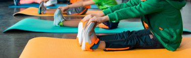 Cropped view of children stretching on fitness mats in sports center, panoramic shot clipart