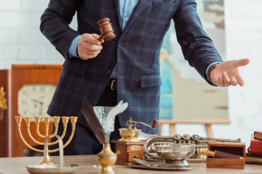 cropped view of auctioneer holding gavel and pointing with hand at antique objects during auction clipart