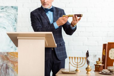 cropped view of auctioneer in suit holding spyglass during auction clipart