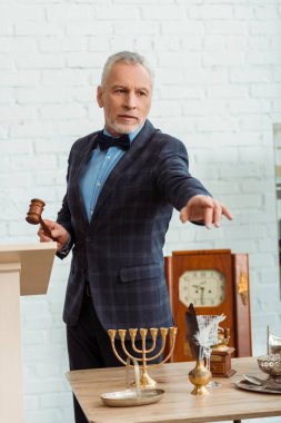 handsome auctioneer holding wooden gavel and pointing with finger during auction clipart